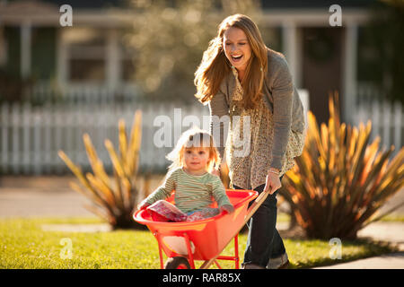 Woman pushing a wheelbarrow with her young daughter inside. Stock Photo