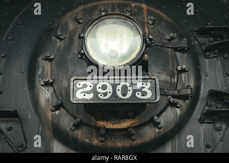 Gritty photo of the front of the boiler of an old steam-powered locomotive with headlight and number plate also visible. Stock Photo