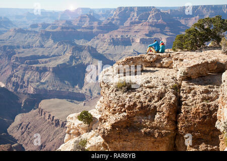 hiker couple sitting at edge of Grand Canyon enjoying the views Stock Photo