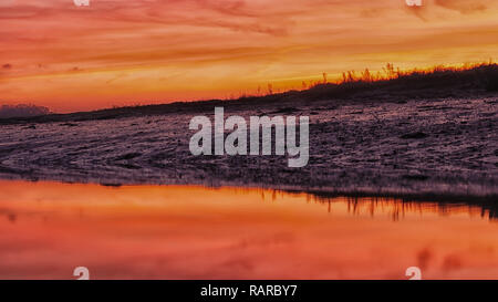 A beautiful landscape of sunset over a low tide river exposing the river bed, with orange sky reflection in the water. Stock Photo