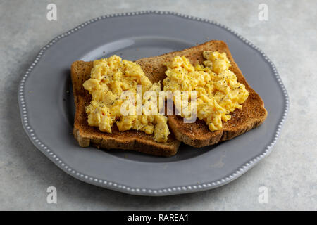 Scrambled eggs with black pepper on two pieces of toast on a grey plate on a simple grey and white marbled background Stock Photo