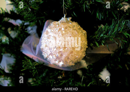 Glittery white ornament on a Christmas tree surrounded by green foliage; close up of Christmas tree decoration. Stock Photo