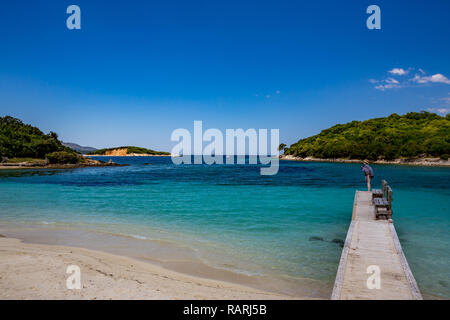 KSAMIL, ALBANIA - MAY 17, 2017:  Female tourist on wooden sea pier with two benches made from pine tree planks enjoys the paradise views at the Albani Stock Photo