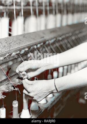 High Point, North Carolina - Textiles. Pickett Yarn Mill. Spinning - Saco-Lowell machine - showing hands of woman in reimagined Stock Photo