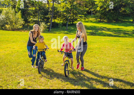 Two happy mothers teach their happy sons to ride a bike Stock Photo