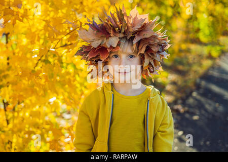 Portrait of little smiling child with wreath of leaves on head background of sunny autumn park Stock Photo