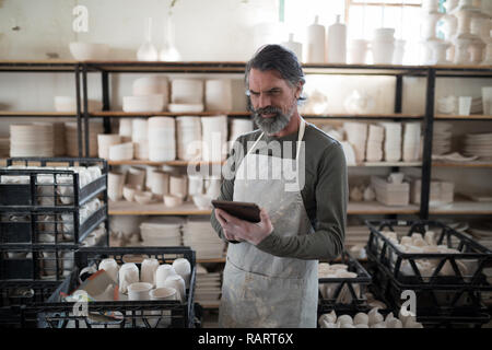 Focused potter using tablet surrounded by work Stock Photo