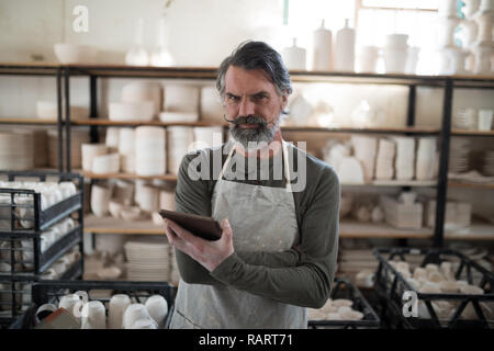 Serious potter using tablet surrounded by work Stock Photo