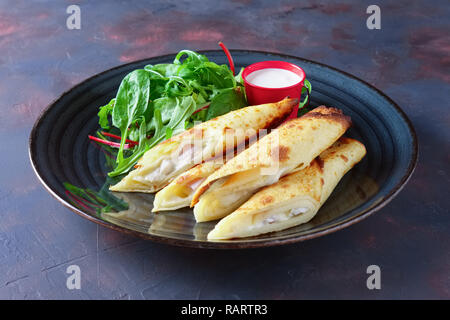 Thin pancakes stuffed with ham and melted cheese served with spinach, arugula, corn and chard salad Stock Photo