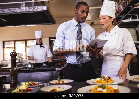 Male manager and female chef using digital tablet in kitchen Stock Photo