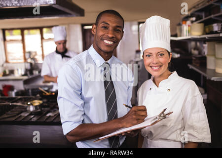 Male manager and female chef writing on clipboard in kitchen Stock Photo