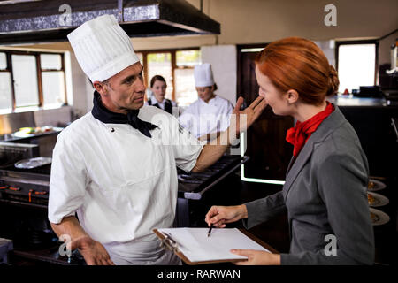 Female manager and male chef interacting with each other in kitchen Stock Photo