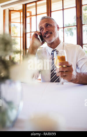 Businessman talking on mobile phone while having white wine Stock Photo