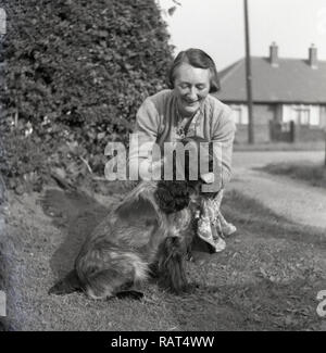 1950s, historical, on a grassy verge, a mature English Lady kneeling beside her pet dog, a Cocker Spaniel. Stock Photo
