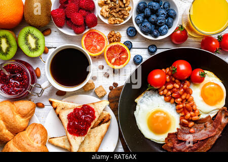 breakfast including coffee, fried egg, bacon, beans, toast, croissant, orange juice with fruits and berries. top view Stock Photo