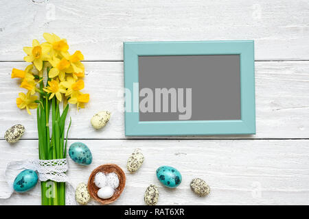 blank photo frame with easter eggs and spring flowers mock up over white wooden table. top view. flat lay Stock Photo