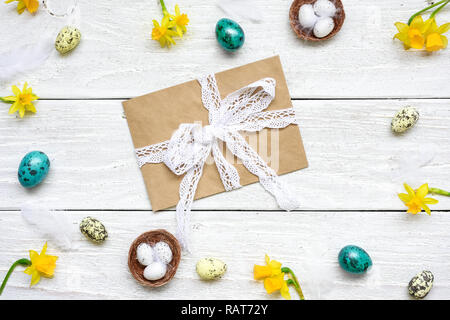 easter greeting card with envelope in frame made of quail eggs, spring flowers and feathers on white wooden background. easter composition. top view w Stock Photo