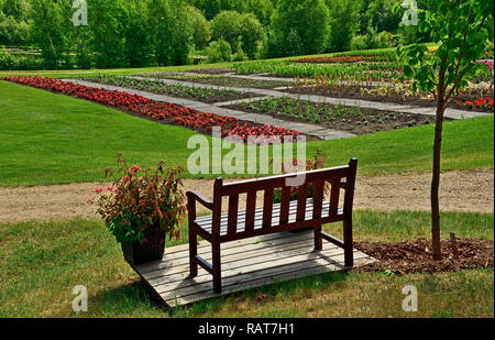 A horizontal landscape image with an empty bench seat overlooking an area thats planted with flowers in the Devonian Gardens near Edmonton Alberta. Stock Photo