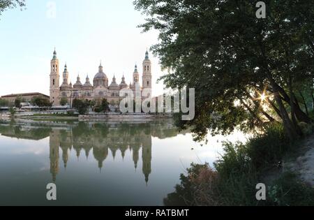 A landscape of christian Pilar Cathedral and Santiago Bridge reflecting in the Ebro river during a sunny summer day in Zaragoza, Aragon region, Spain Stock Photo