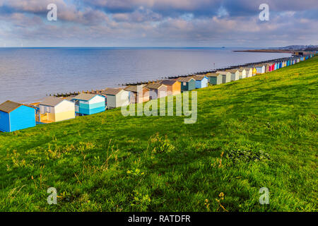 Row of beach huts along the coast in Tankerton, Whitstable, Kent. The green grass slopes are behind the huts and groynes, water breakers can be seen a Stock Photo