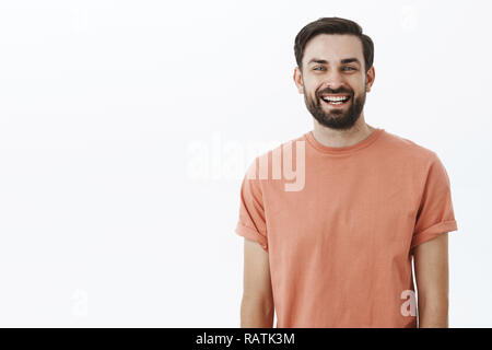 Waist-up shot of bright and cheerful emotive friendly bearded 30s man with broad smile gazing satisfied and upbeat at camera as posing in pink t-shirt over gray background, amused and enthusiastic Stock Photo