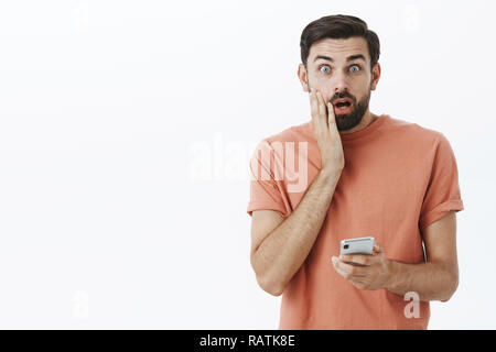 Oh no, wrong number. Portrait of man accidently sent message via smartphone wrong person touching face and open mouth troubled and concerned standing shocked, holding mobile phone in hand Stock Photo
