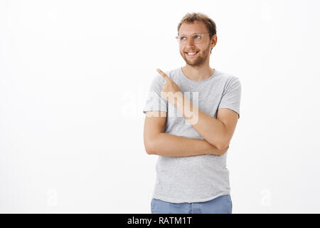 Dreamy and creative ambitious male entrepreneur standing over white background pointing and gazing at upper left corner with pleased happy smile feeling delight and satisfaction enjoying nice view Stock Photo