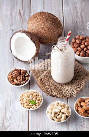 Vegan milk from nuts in the bottle with red stripped straw around various nuts on white wooden table Stock Photo