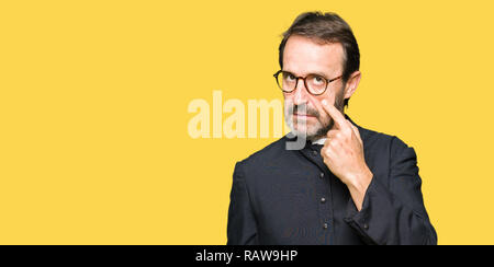 Middle age priest man wearing catholic robe Pointing to the eye watching you gesture, suspicious expression Stock Photo