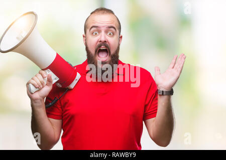 Young caucasian man shouting through megaphone over isolated background very happy and excited, winner expression celebrating victory screaming with b Stock Photo
