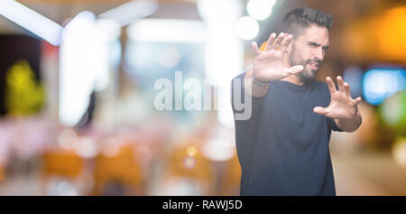 Young handsome man wearing sweater over isolated background afraid and terrified with fear expression stop gesture with hands, shouting in shock. Pani Stock Photo
