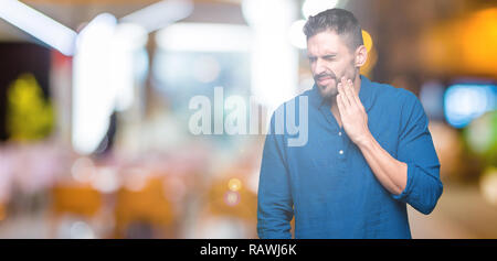 Young handsome man over isolated background touching mouth with hand with painful expression because of toothache or dental illness on teeth. Dentist  Stock Photo