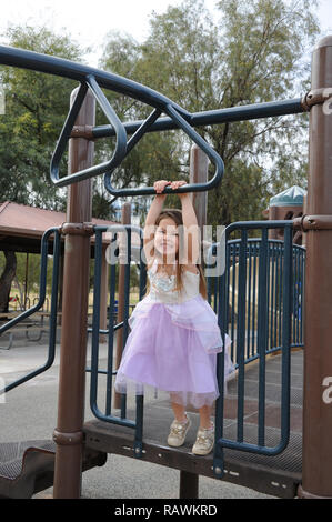 Young Girl Playing on Monkey Bars Playground in a Princess Dress Stock Photo