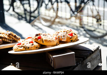 Delicious chocolate chip cookies on display in the sunshine at coffee shop with a view of a bicycle through the window Stock Photo