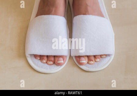 Closeup top view of pair of white new slippers in room of hotel. Woman with beautiful french white and pink fresh pedicure. Horizontal color photograp Stock Photo