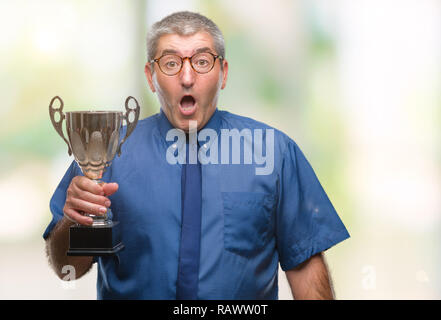 Handsome senior successful man holding trophy over isolated background scared in shock with a surprise face, afraid and excited with fear expression Stock Photo
