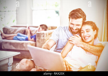 Happy couple sitting on sofa and using laptop Stock Photo