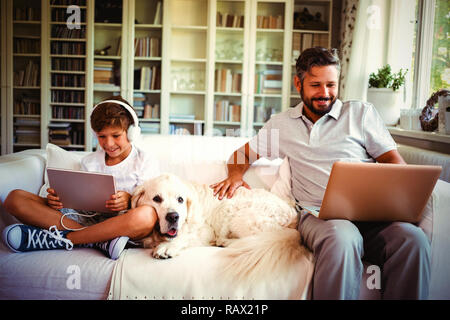 Father and son sitting on sofa and using digital tablet and laptop Stock Photo