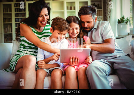 Parents with their children sitting on sofa and using digital tablet Stock Photo