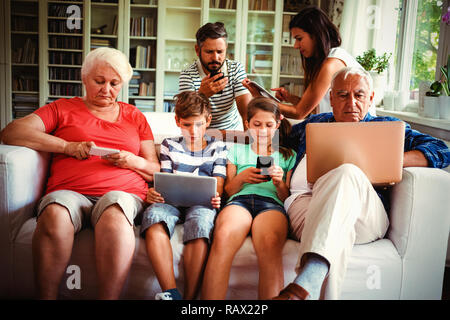Multi-generation family sitting on sofa and using various technologies Stock Photo