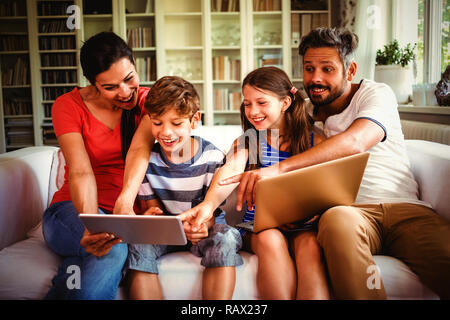 Cheerful family using technologies while sitting on sofa Stock Photo