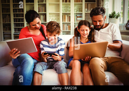 Family using various technologies while sitting on sofa Stock Photo