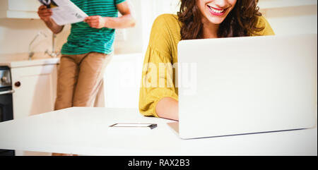 Woman using laptop while man reading newspaper in background Stock Photo