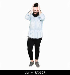 Young hipster man with long hair and beard wearing glasses suffering from headache desperate and stressed because pain and migraine. Hands on head.