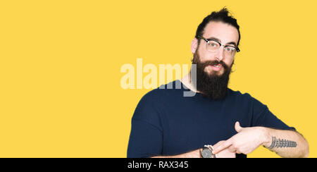 Young hipster man with long hair and beard wearing glasses In hurry pointing to watch time, impatience, upset and angry for deadline delay Stock Photo