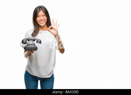 Young asian woman holding vintagera telephone over isolated background doing ok sign with fingers, excellent symbol Stock Photo
