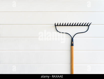 Minimalist image of new rake hanging on clean white wooden texture wall with copy space Stock Photo