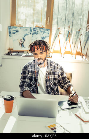Young creative artist drinking some coffee and working on laptop Stock Photo