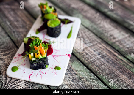 Raw vegan sushi rolls with vegetables and green sauce with food styling in restaurant