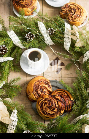 Snail chocolate muffins served with coffee on the background of a wreath of fir branches and cones. Rustic style. Stock Photo